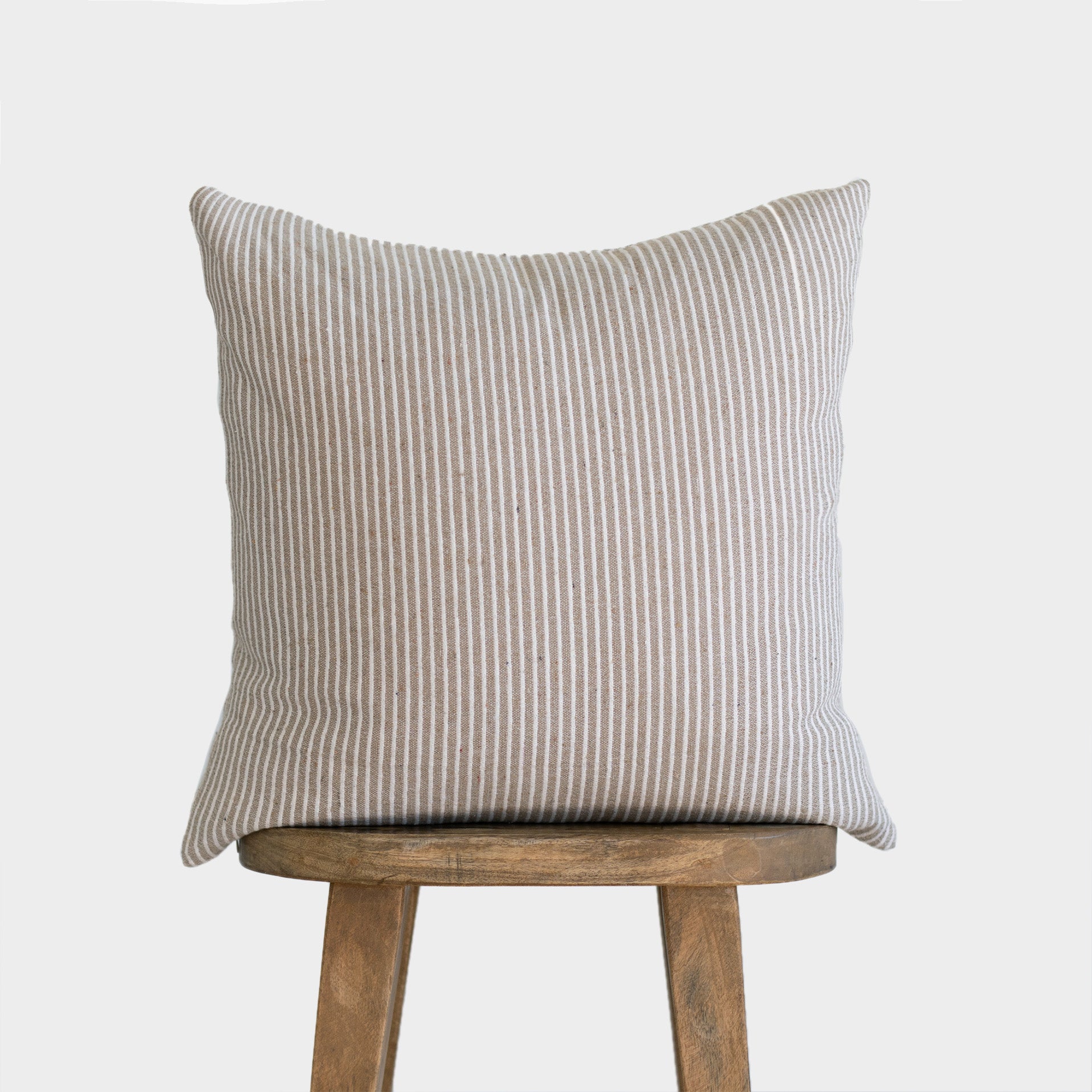 Tan and white striped throw pillow displayed on a wooden stool against a white background.