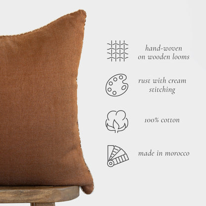 Rust-brown textured cotton pillow with cream stitching detail on wooden base.