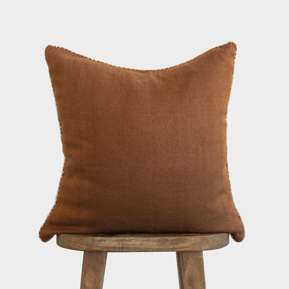 Brown throw pillow with whipstitched edges displayed on wooden stool.