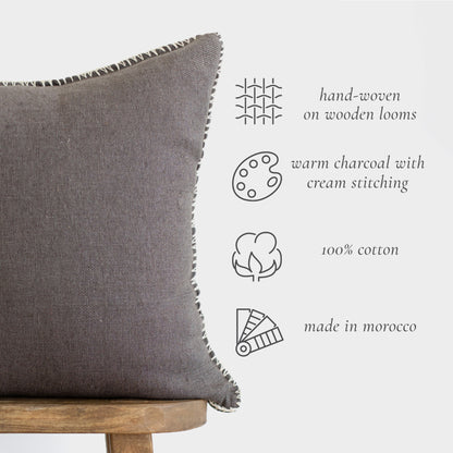 Charcoal cotton throw pillow with cream whipstitched edges on wooden stool.