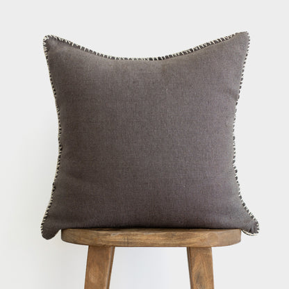 Charcoal gray pillow with whipstitched edges, displayed on wooden stool.