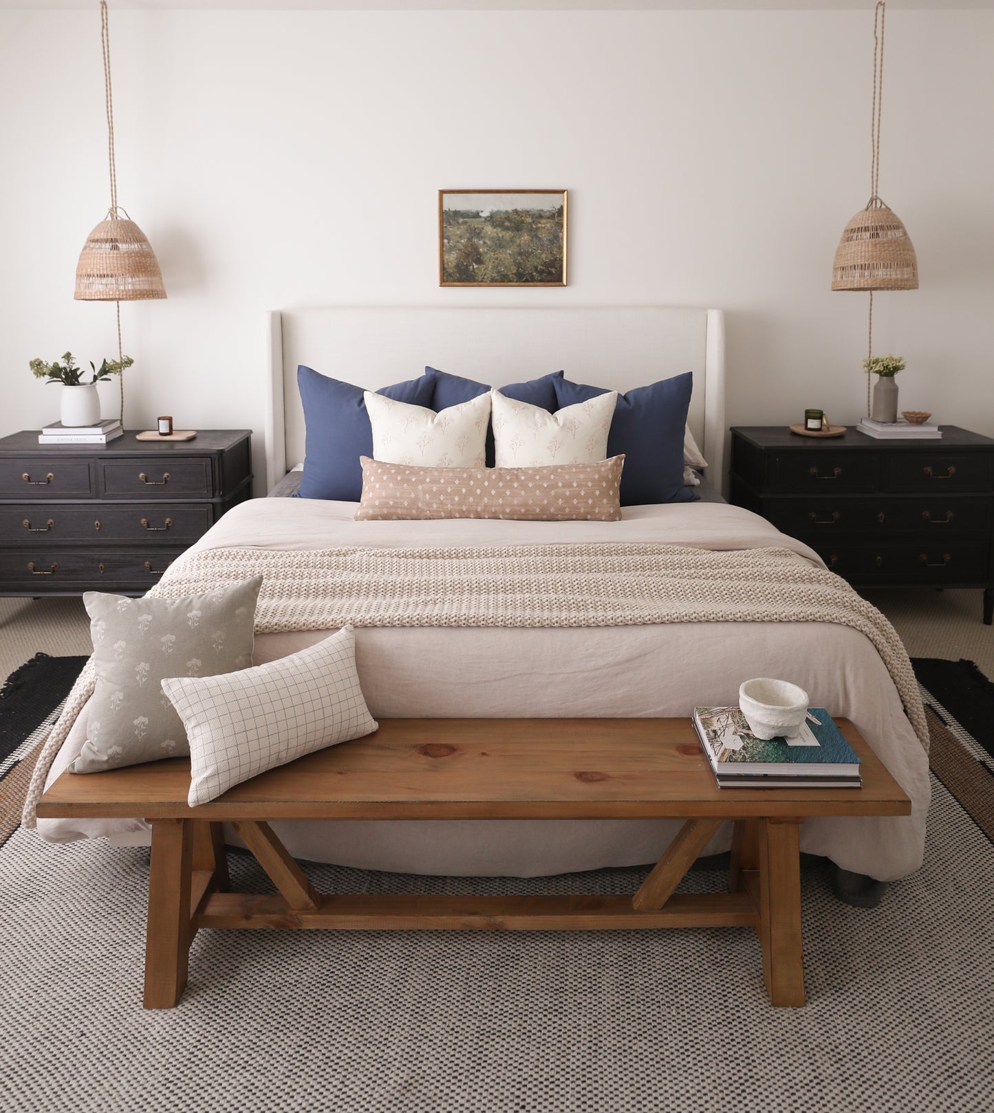 Navy blue and cream pillows arranged on bed with white headboard and beige bedding.