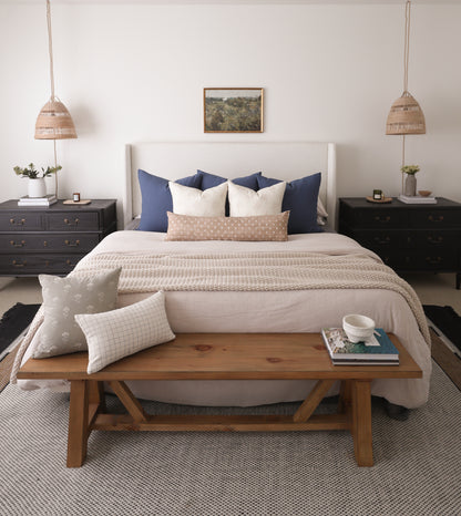 Navy blue and cream pillows arranged on bed with white headboard and beige bedding.