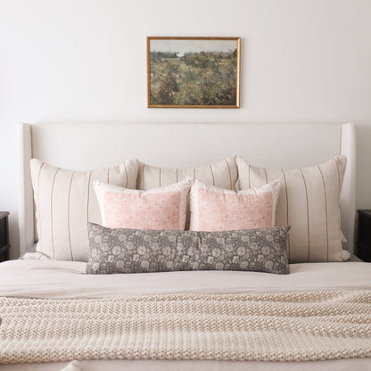 Rectangular lumbar pillow with gray floral pattern displayed on bed with striped and pink pillows.