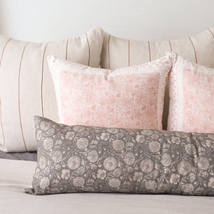 Gray rectangular lumbar pillow with white floral pattern, displayed with pink and cream striped pillows on a bed.