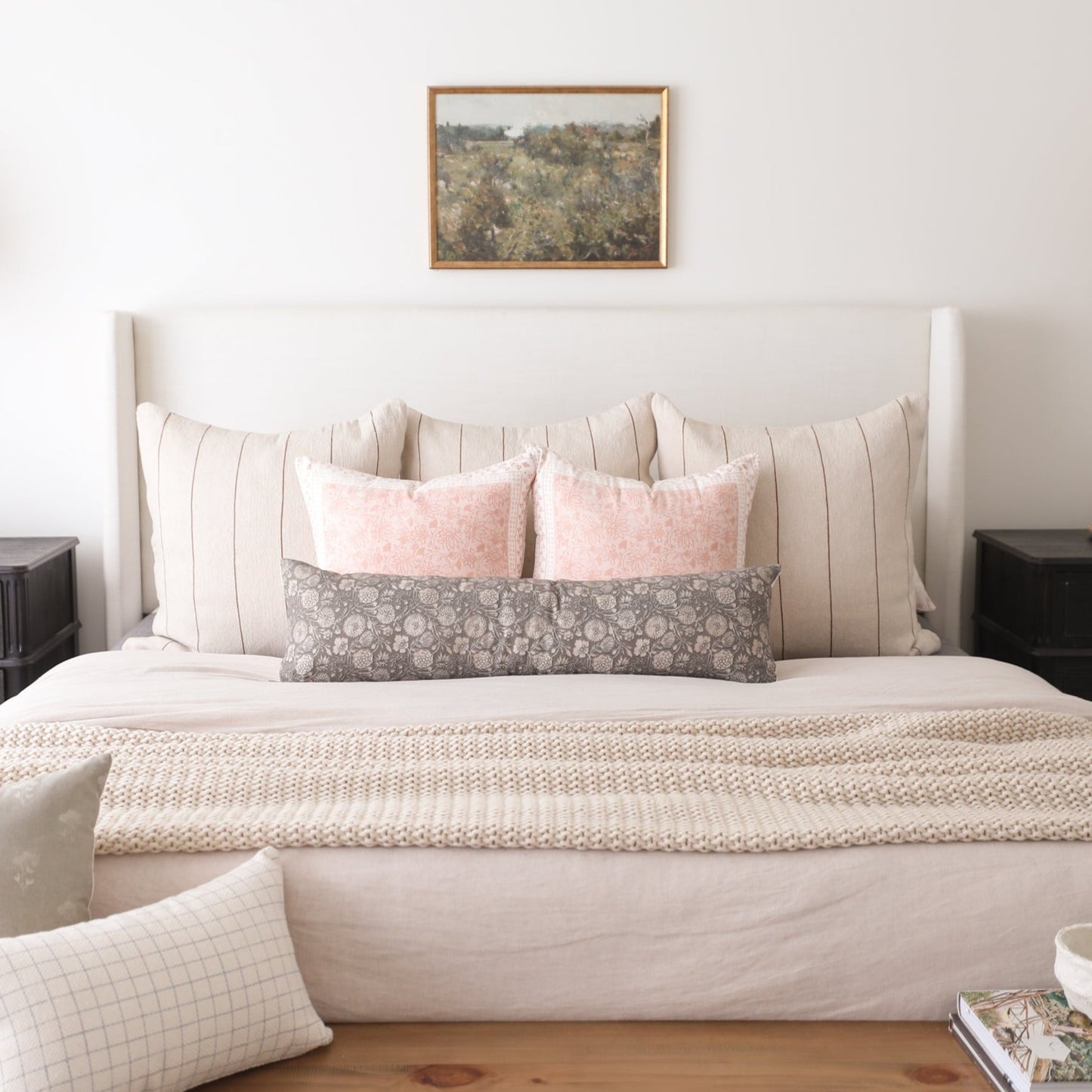 Gray floral lumbar pillow displayed on a bed with pink and striped pillows and neutral bedding.