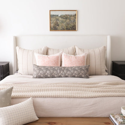 Framed landscape artwork with brown wooden frame hung above a bed with neutral pillows and bedding.