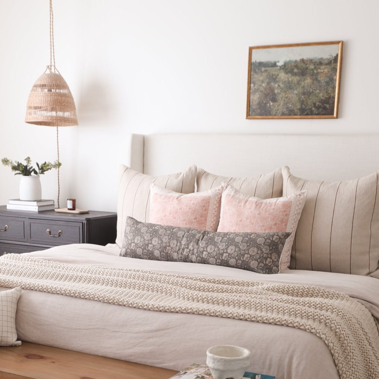 Ives pillow in pink and gray floral patterns displayed on a bed with neutral bedding and striped headboard.