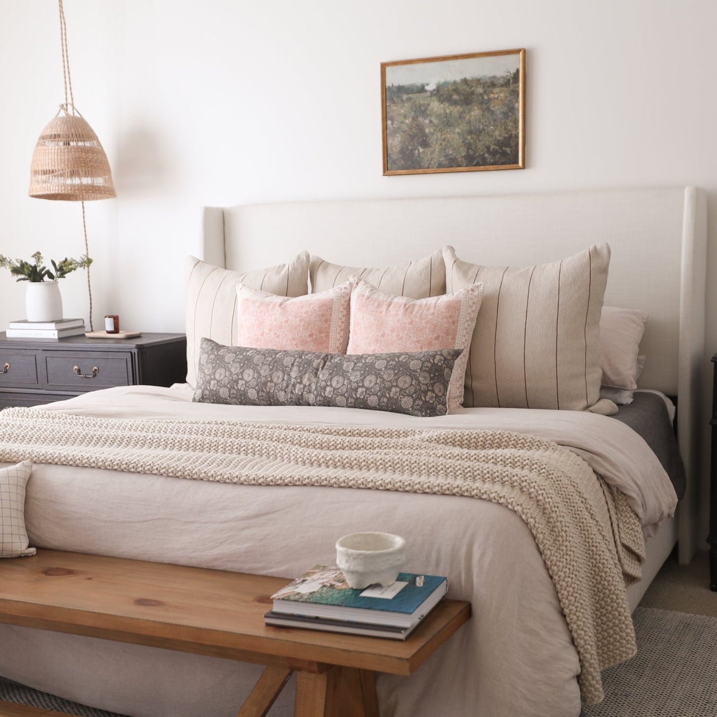 Framed landscape art print with wood border hanging above a bed with neutral pillows and bedding.