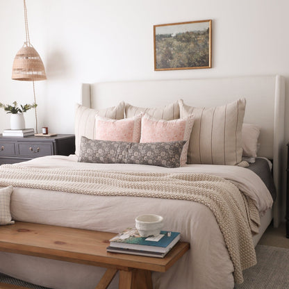 Framed landscape art print with wood border hanging above a bed with neutral pillows and bedding.