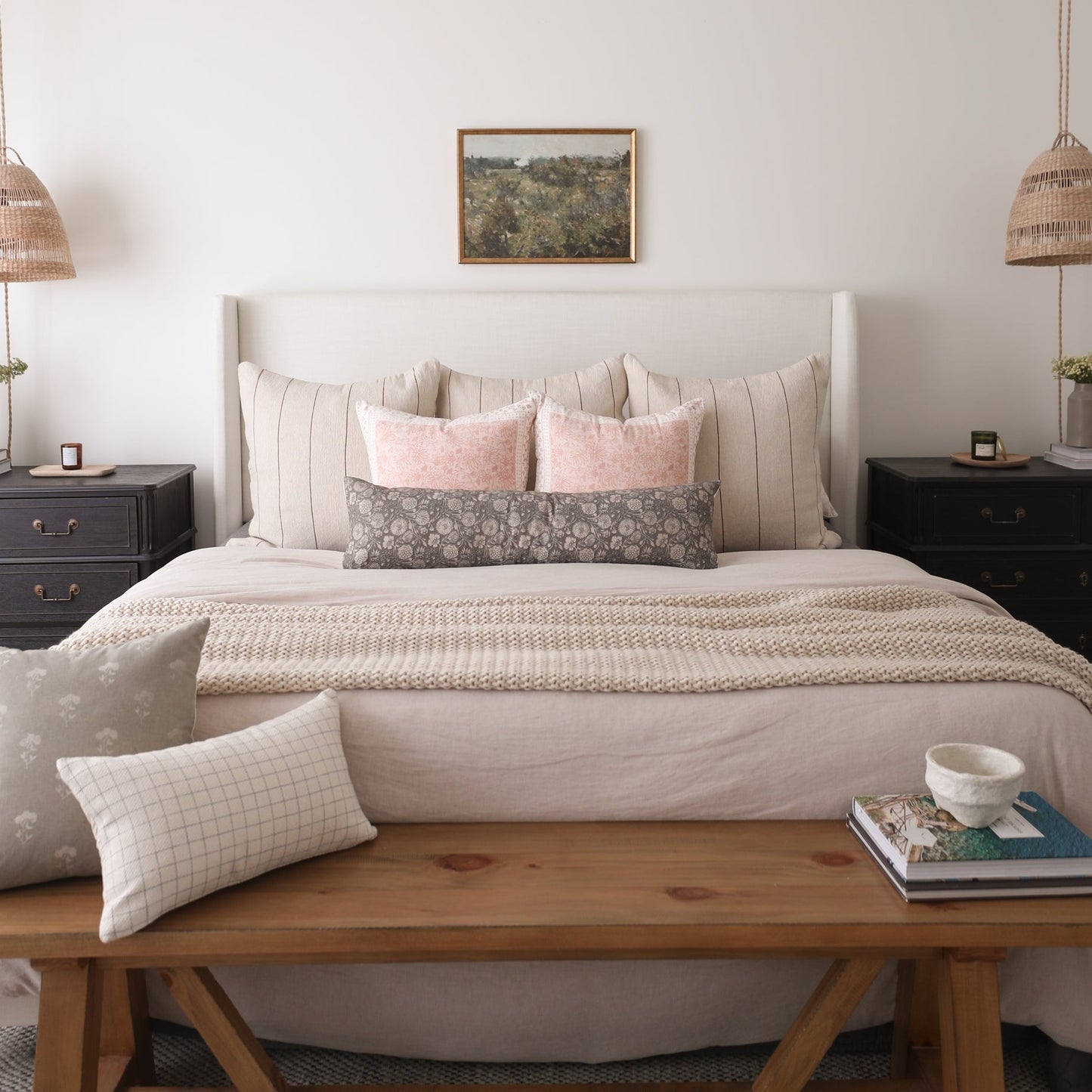 Upholstered bed with gray headboard, layered pillows in cream and pink tones, and beige textured bedding in bedroom setting.
