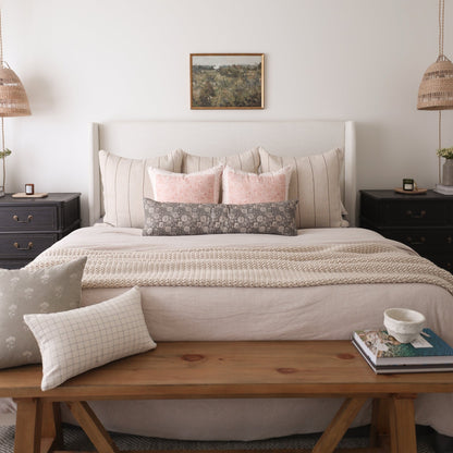 Upholstered bed with gray headboard, layered pillows in cream and pink tones, and beige textured bedding in bedroom setting.