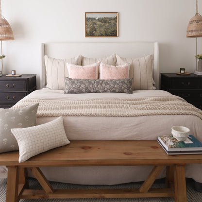 Rectangular lumbar pillow with gray floral pattern displayed on a bed with pink and neutral pillows.