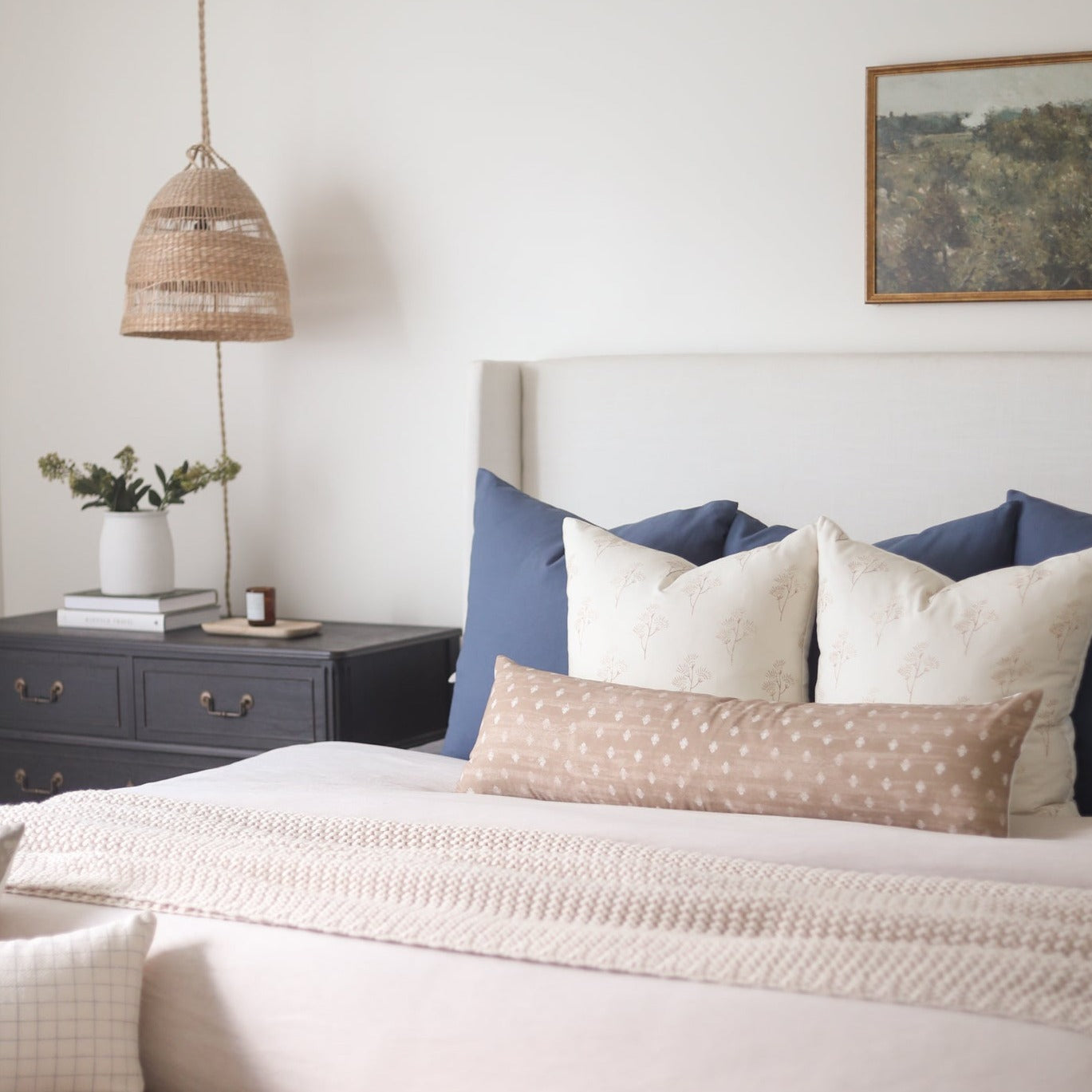Navy blue and cream decorative pillows arranged on a bed with a woven headboard.
