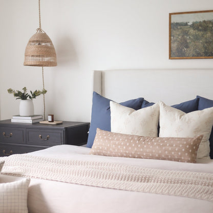 Navy blue and cream decorative pillows arranged on a bed with a woven headboard.