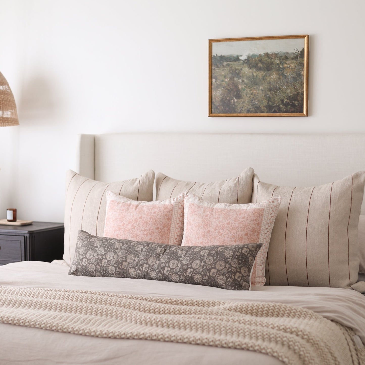 Rectangular lumbar pillow with gray floral pattern displayed on bed with pink and striped pillows.