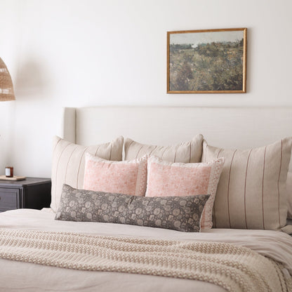 Rectangular lumbar pillow with gray floral pattern displayed on bed with pink and striped pillows.