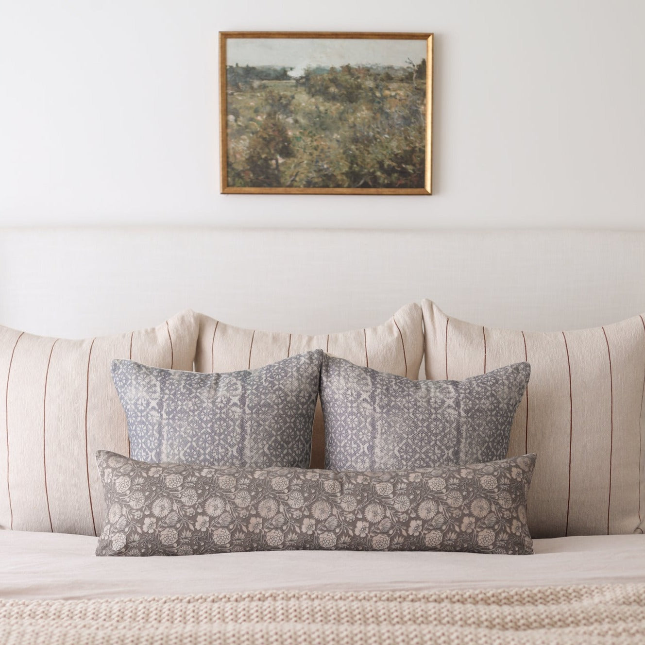 Rectangular lumbar pillow with gray floral pattern displayed on bed with matching square pillows.