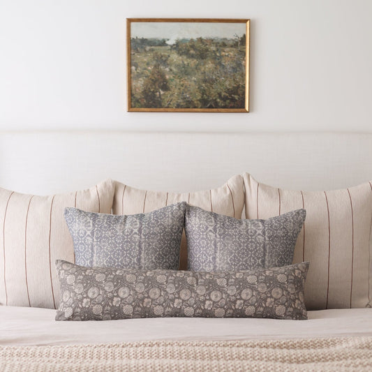 Rectangular lumbar pillow with gray floral pattern displayed on bed with matching square pillows.