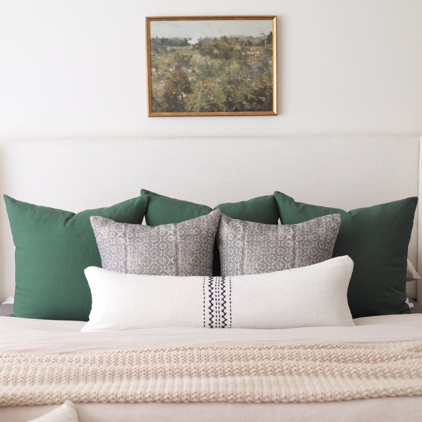 White lumbar pillow with black diamond pattern band, displayed on bed with green and patterned pillows.