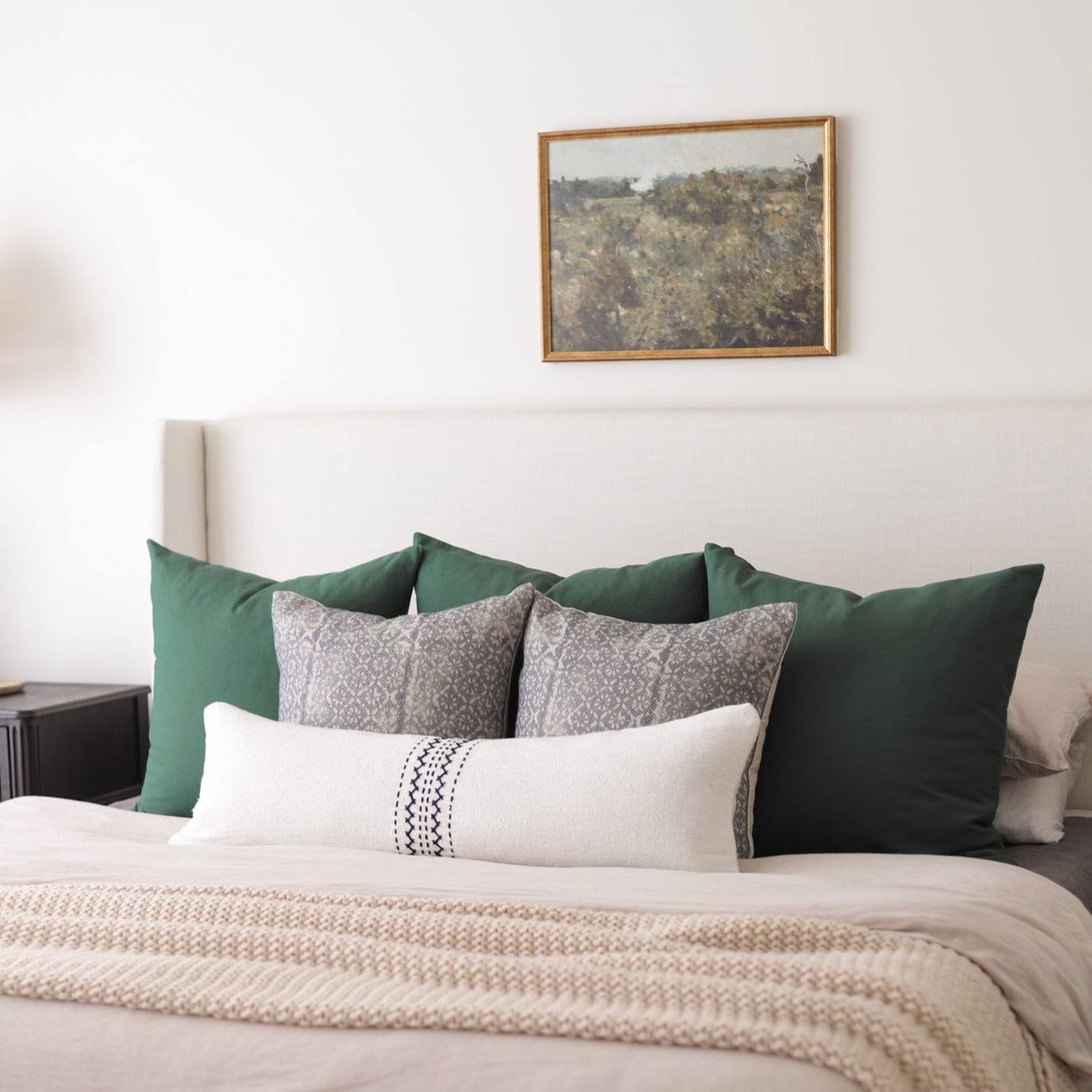 Pine wood frame with landscape artwork hung above bed with green and patterned pillows.