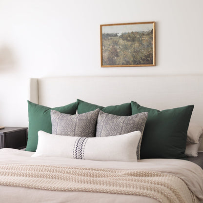 Pine wood frame with landscape artwork hung above bed with green and patterned pillows.