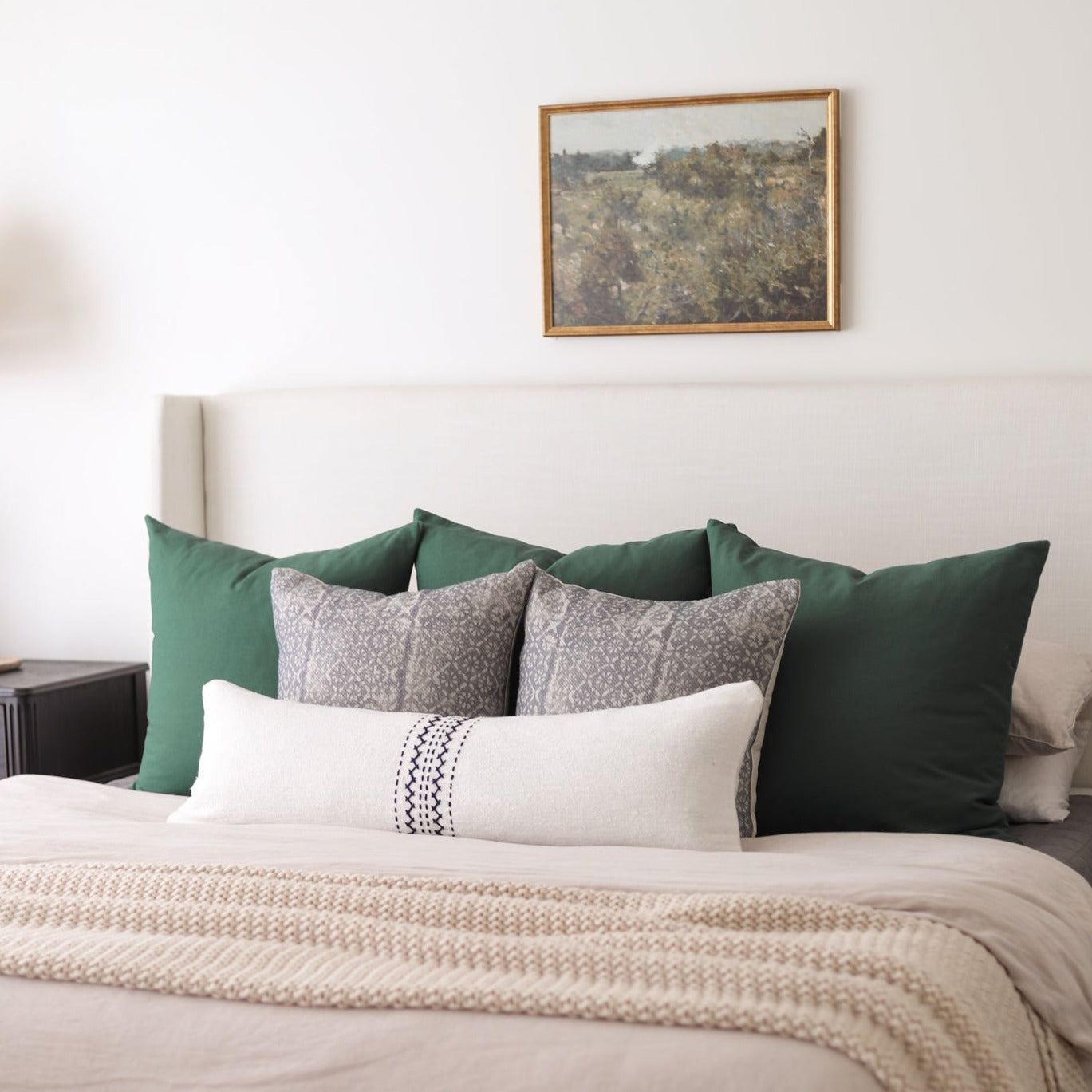 Cream lumbar pillow with black diamond pattern detail on a styled bed with green and patterned pillows.
