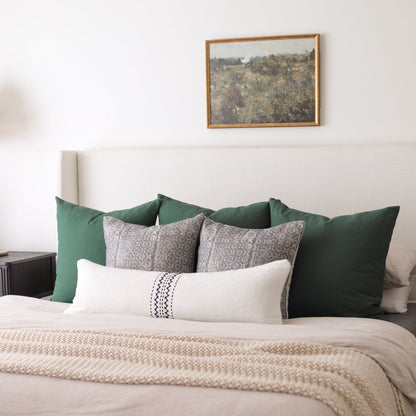 Cream lumbar pillow with black diamond pattern detail on a styled bed with green and patterned pillows.