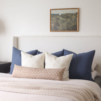 Navy, cream, and taupe decorative pillows arranged on a bed with white bedding.
