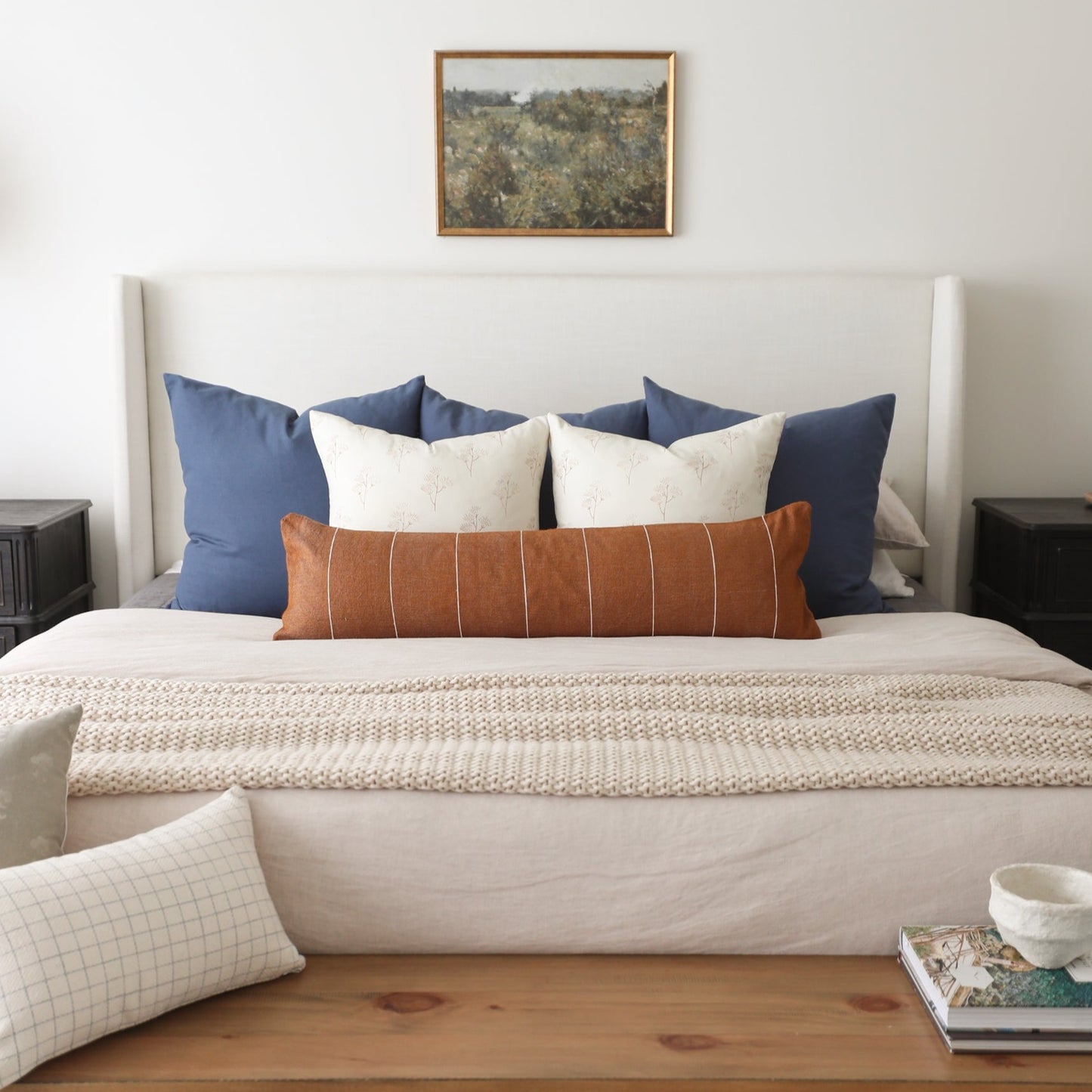 Bed styled with navy blue pillows, cream patterned pillows, and terracotta lumbar pillow with white stitching.