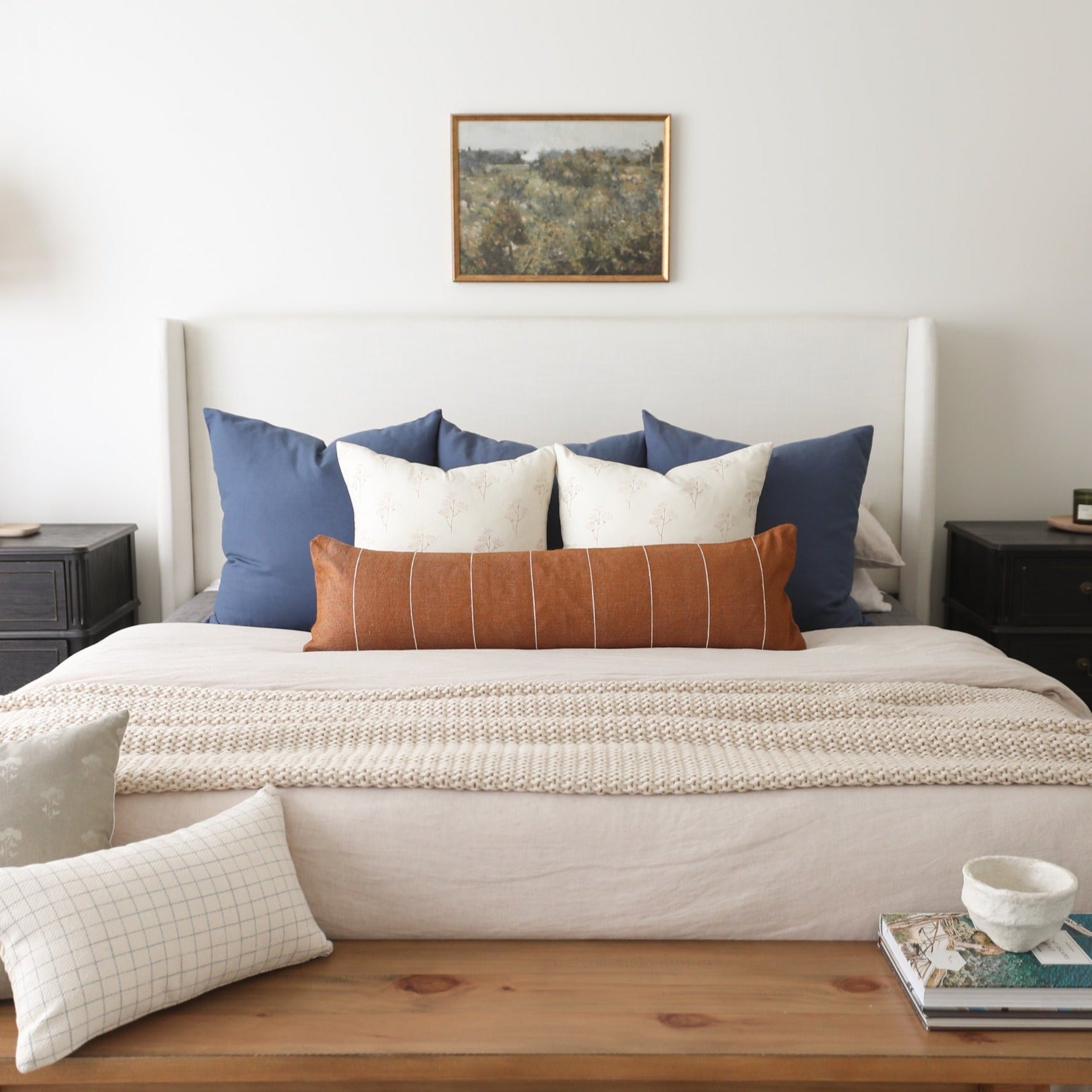 Navy blue and cream decorative pillows arranged on a bed with a rust-colored striped lumbar pillow in the center.