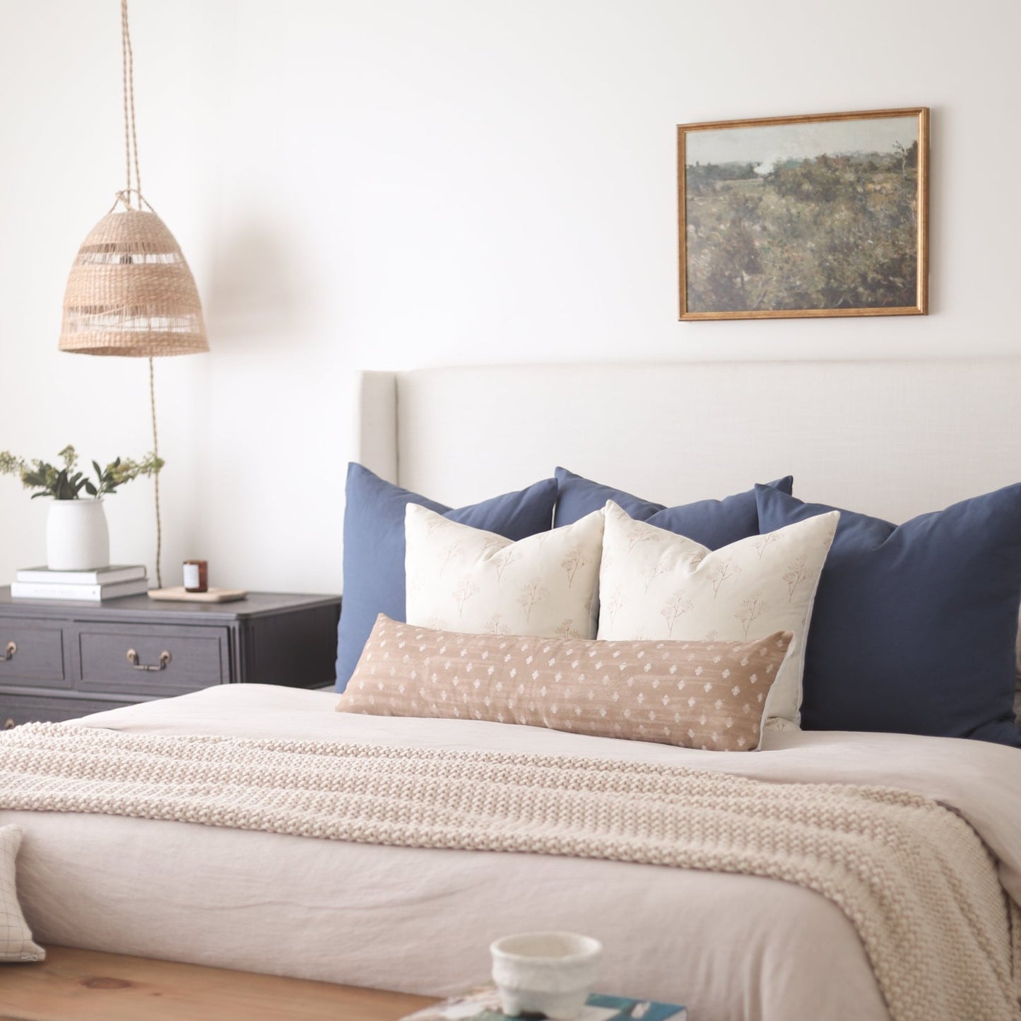 Navy, cream, and tan patterned pillows arranged on a bed with navy headboard and beige bedding.
