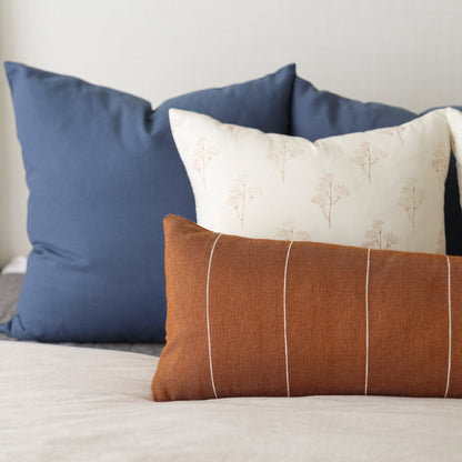 Three decorative pillows in navy, cream with botanical pattern, and brown with vertical stripes.