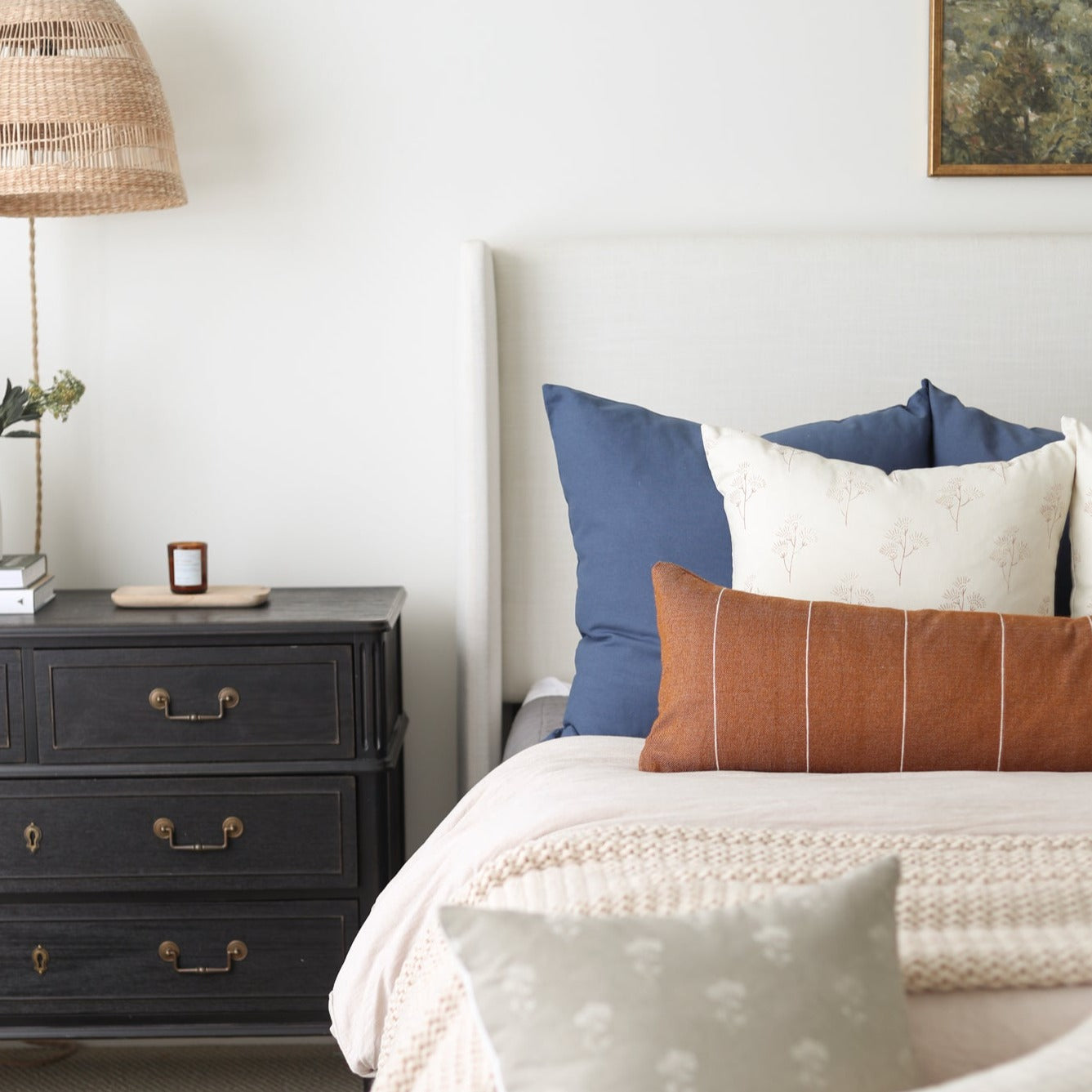 Navy blue and cream decorative pillows arranged on a bed with white bedding and tan knit throw.
