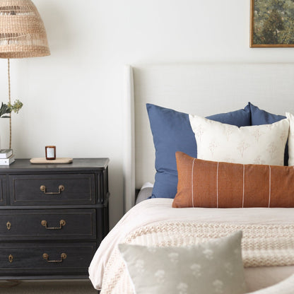 Navy blue and cream decorative pillows arranged on a bed with white bedding and tan knit throw.