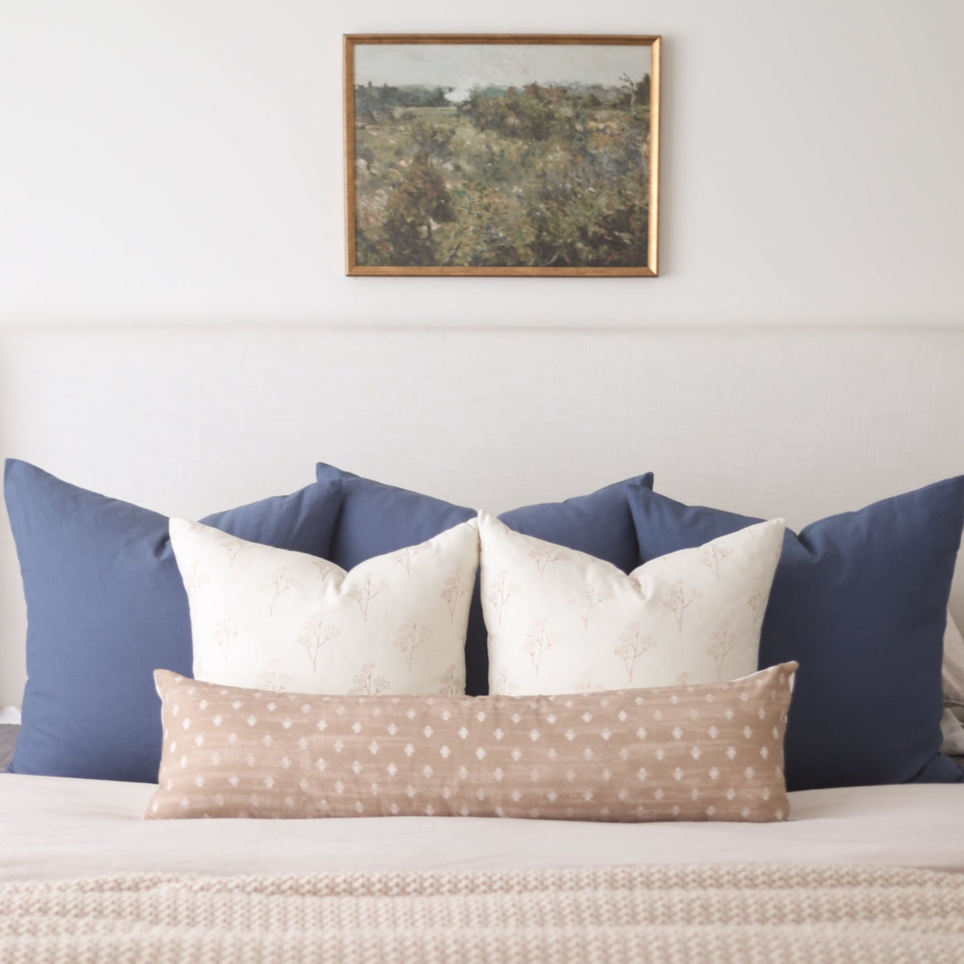 Bed arrangement with navy, cream, and tan patterned pillows in various sizes against white bedding.