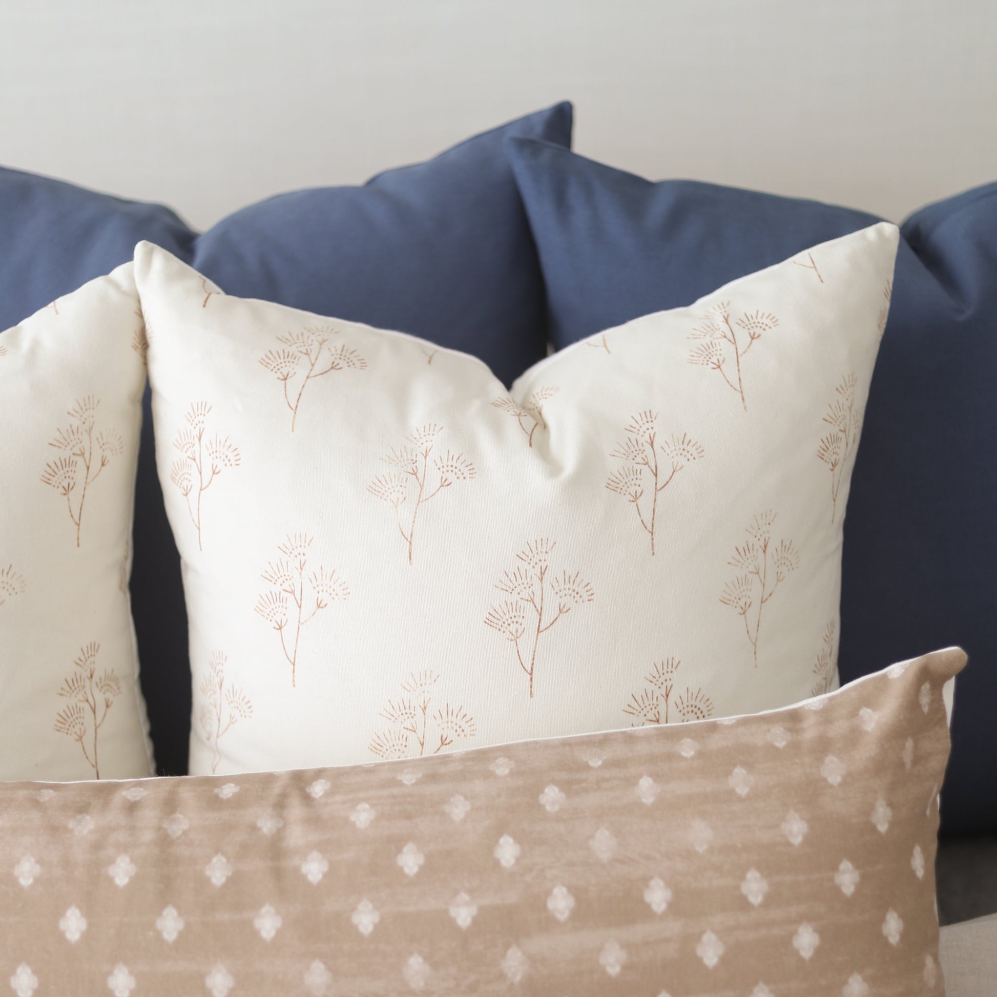 Cream pillows with tan botanical print and tan pillow with white diamond pattern, displayed against navy pillows.