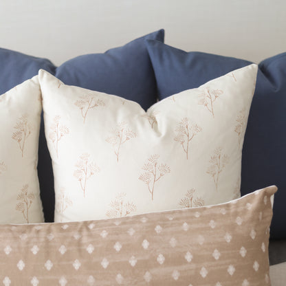 Cream pillows with tan botanical print and tan pillow with white diamond pattern, displayed against navy pillows.