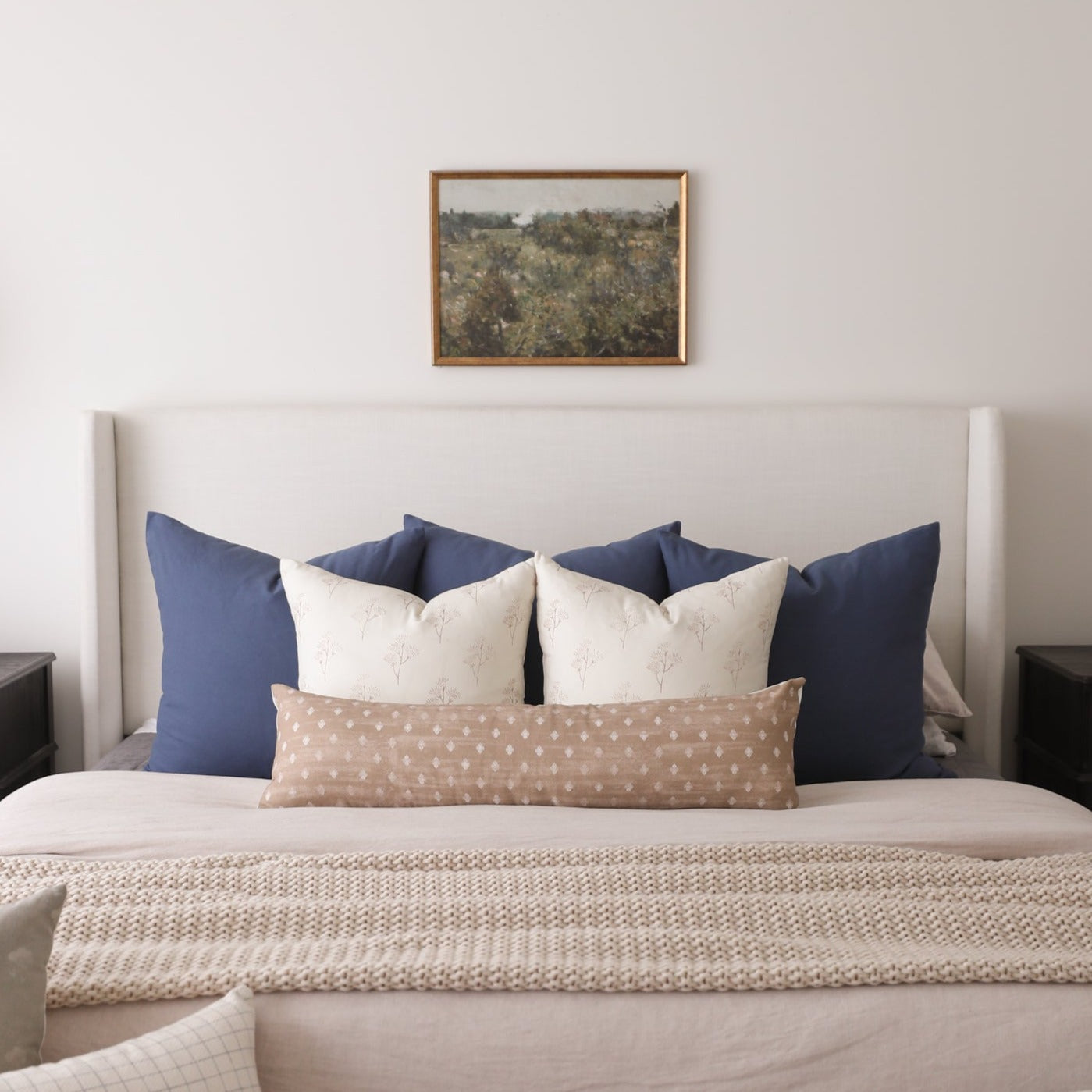 Navy and cream decorative pillows arranged on a bed with a beige headboard and textured throw blanket.