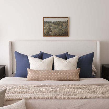 Navy and cream decorative pillows arranged on a bed with a beige headboard and textured throw blanket.