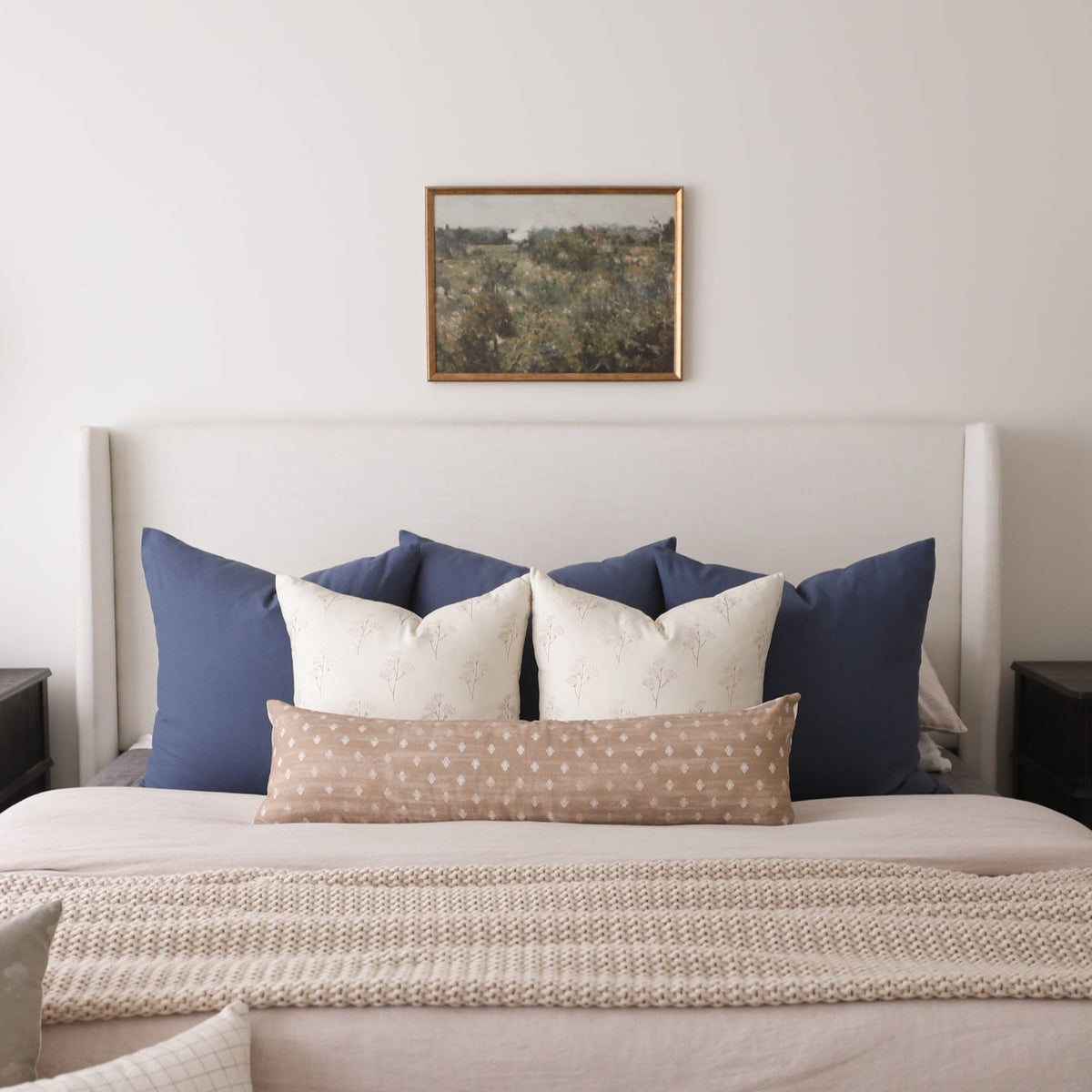 Rectangular pillow with tan background and white dot pattern, displayed on a bed with blue and cream pillows.