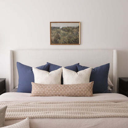 Rectangular pillow with tan background and white dot pattern, displayed on a bed with blue and cream pillows.