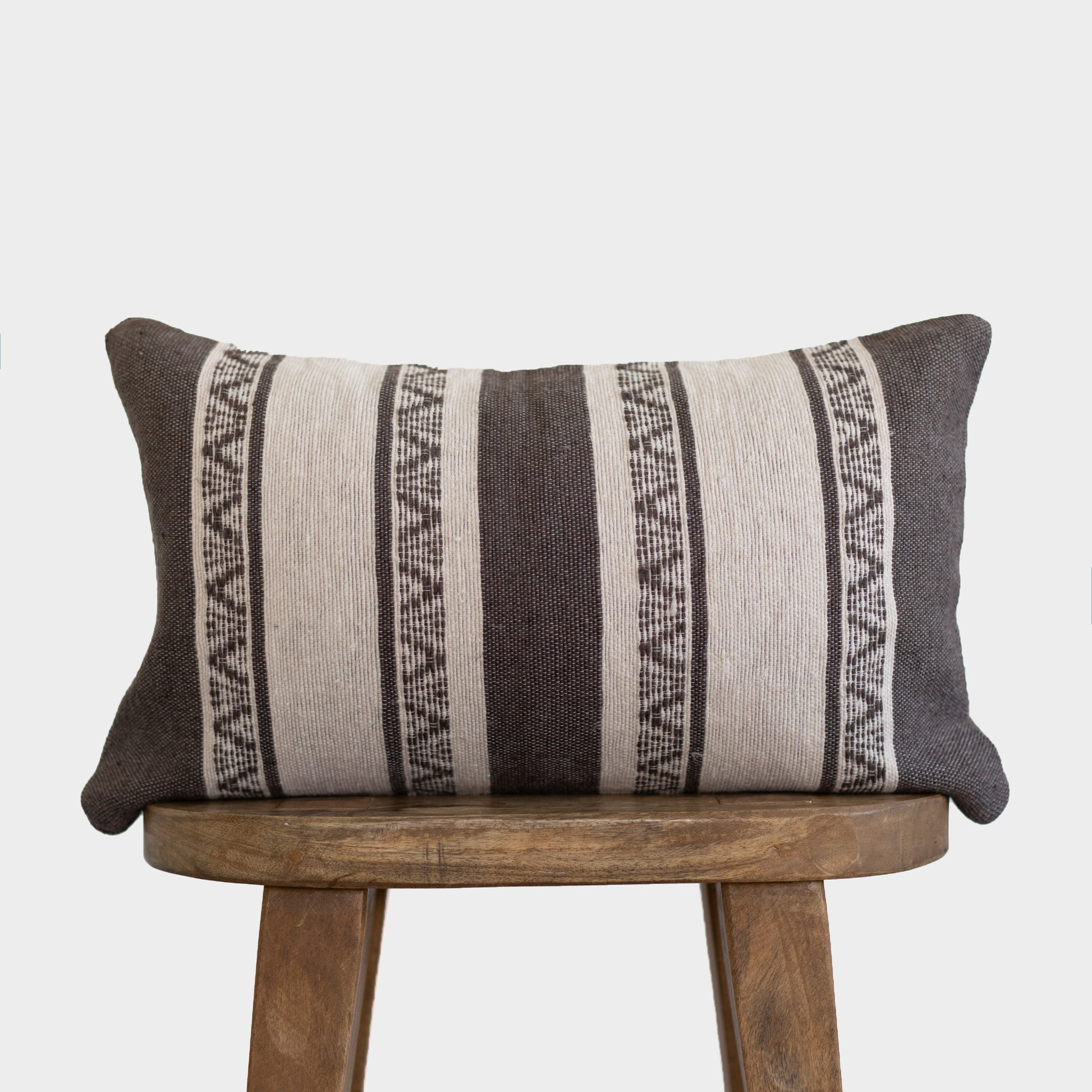 Charcoal and cream striped lumbar pillow with geometric patterns on wooden stool.