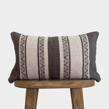 Charcoal and cream striped lumbar pillow with geometric patterns on wooden stool.