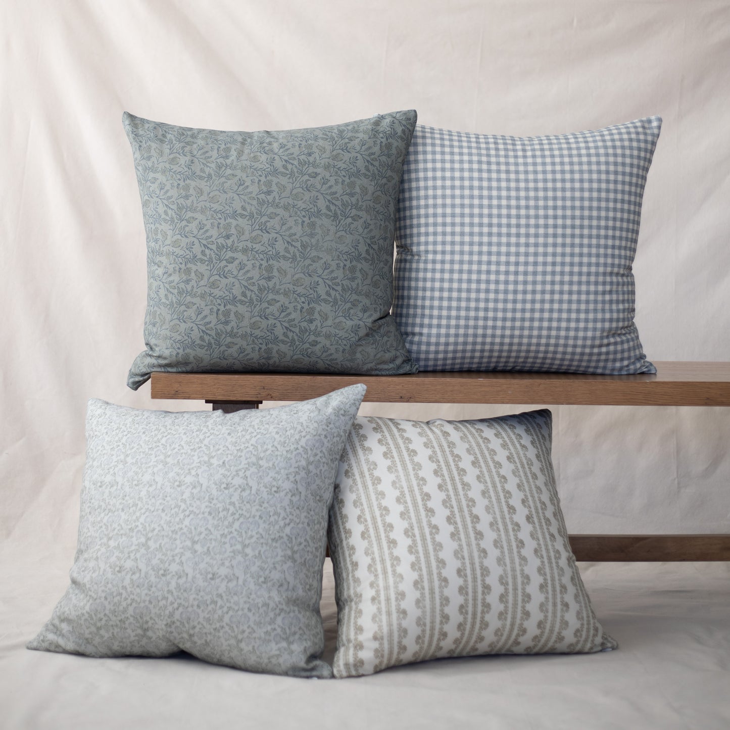 Four throw pillows in varying patterns: floral, gingham, textured, and striped designs in blue and gray tones.