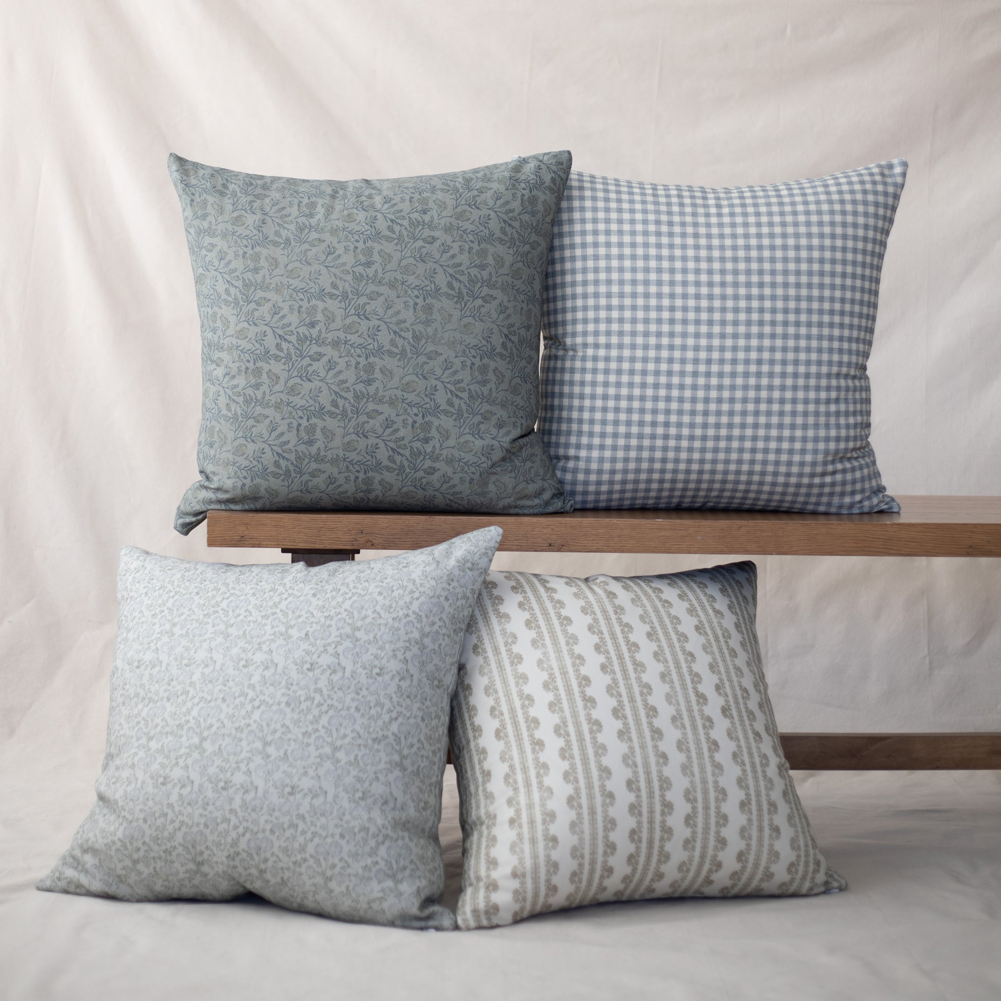 Four throw pillows in varying patterns: floral, gingham, textured, and striped designs in blue and gray tones.
