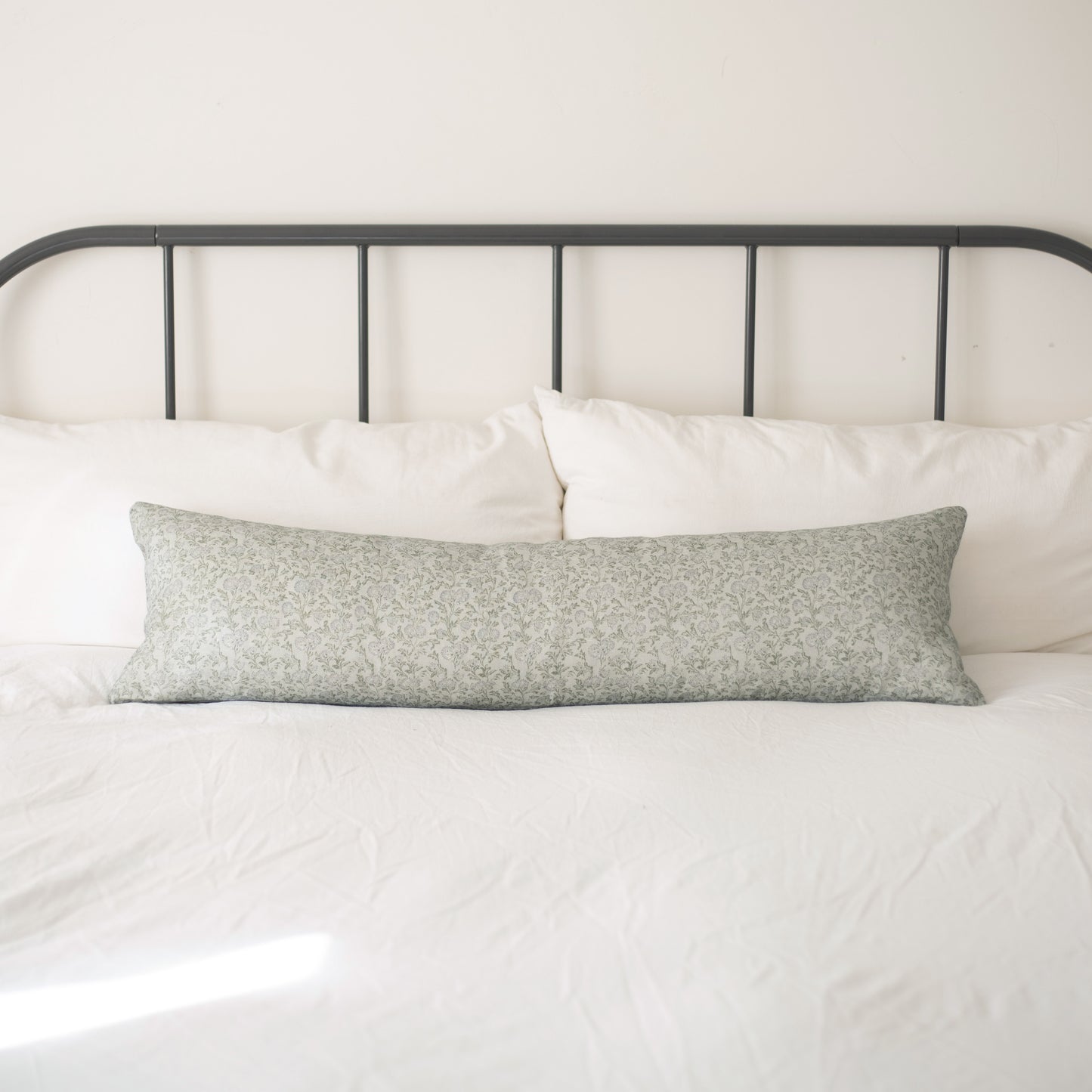 Sage green patterned linen lumbar pillow on a bed with white bedding and dark metal headboard.