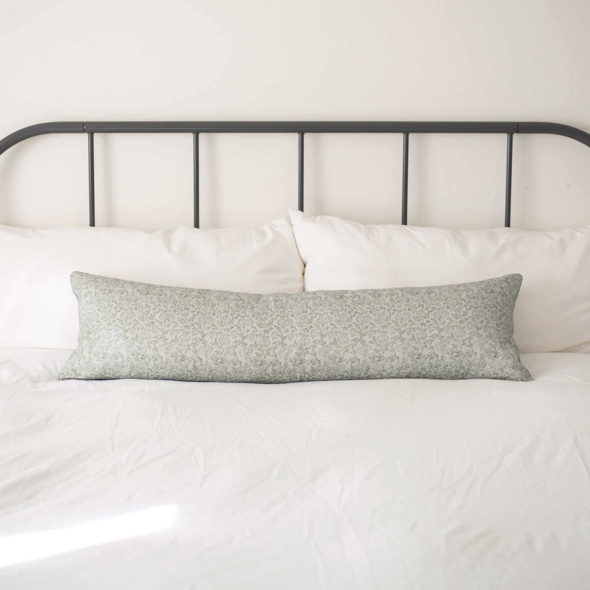 Sage green patterned linen lumbar pillow on a bed with white bedding and dark metal headboard.