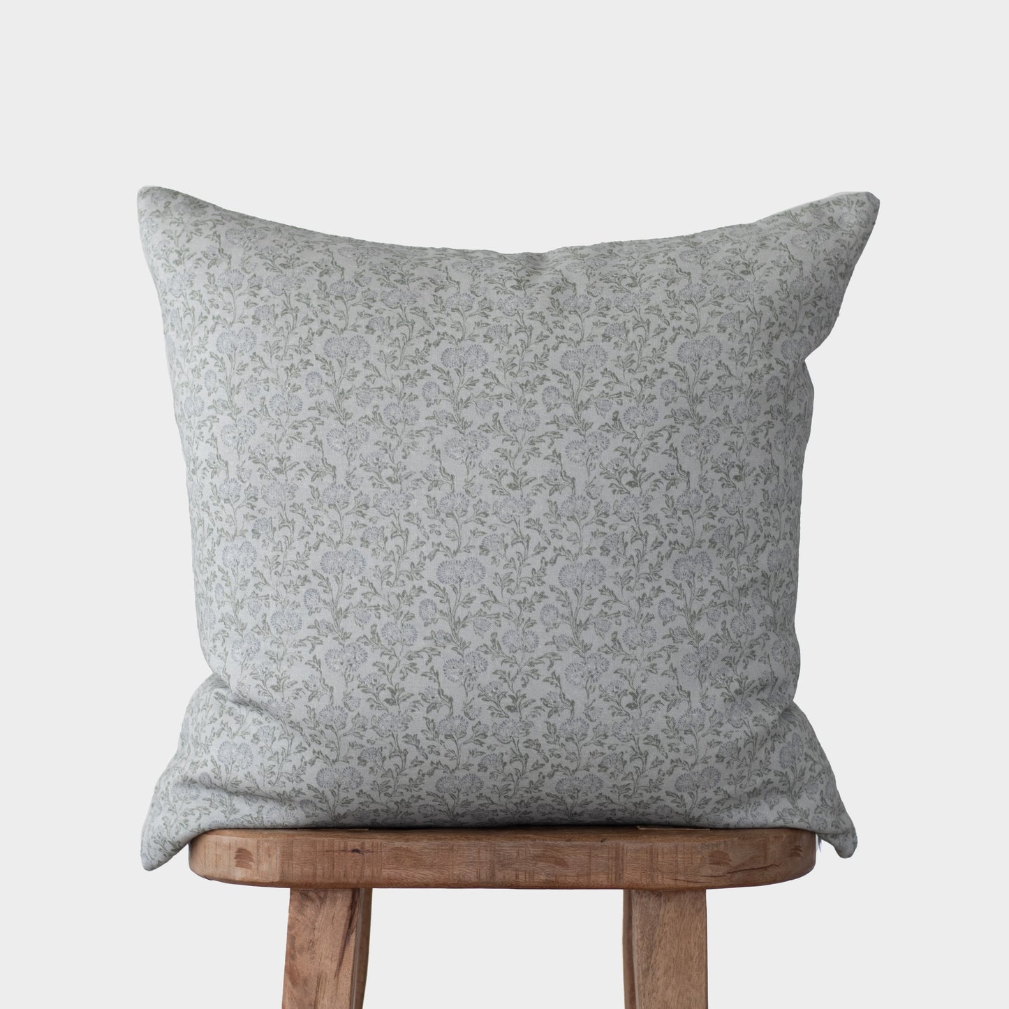Gray linen pillow with delicate floral pattern resting on wooden chair.