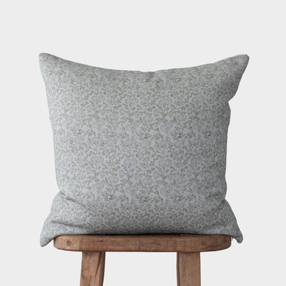 Gray linen pillow with delicate floral pattern resting on wooden chair.